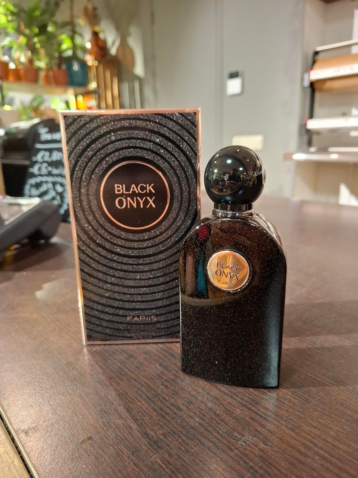 Het parfumflesje Black Onyx en de bijbehorende glinsterende zwarte doos met gouden letters staan op een houten toonbank.