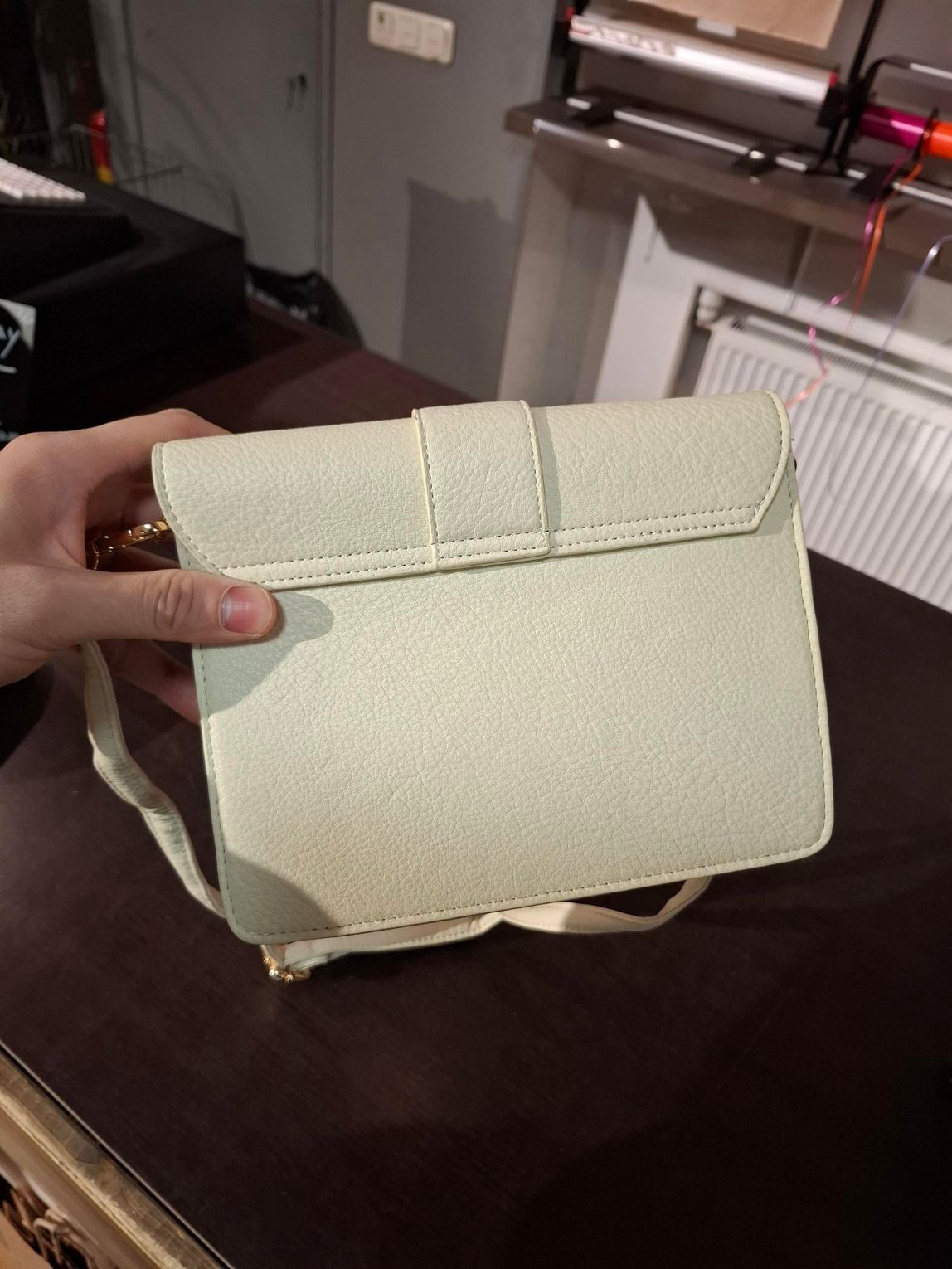 Hand die een crèmekleurige, gewatteerde handtas vasthoudt in een kledingwinkel.