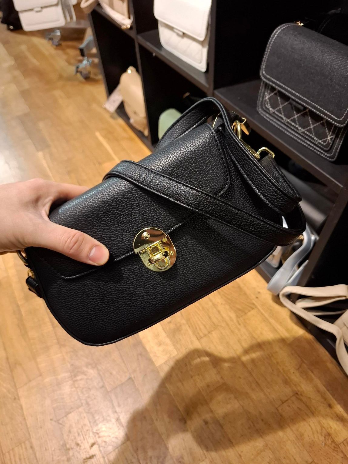 Hand die een klein zwart, gestructureerd handtasje met gouden sluiting vasthoudt in een boetiek.