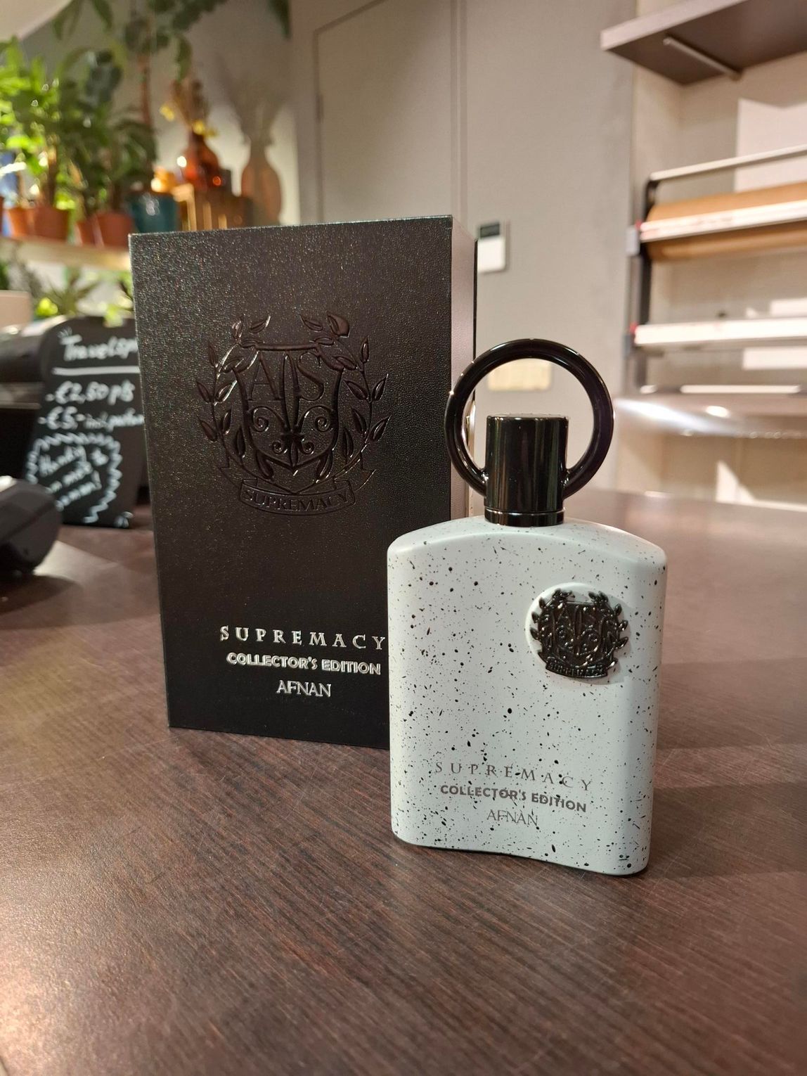 Een flesje Afnan Supremacy Incense parfum en de bijbehorende zwarte, gestructureerde doos staan op een houten tafel in een winkelomgeving.