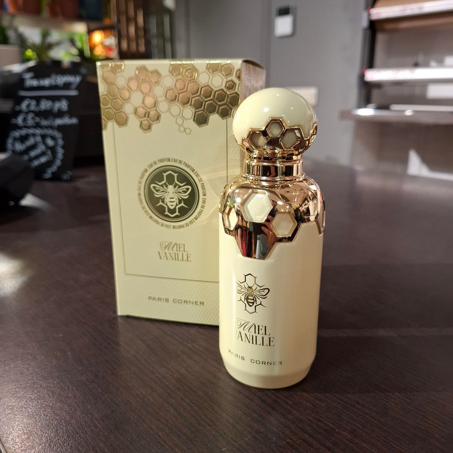 Een fles Jean Paul Gaultier Divine Le Parfum parfum en de bijbehorende beige doos met gouden honingraatmotief op een tafel.