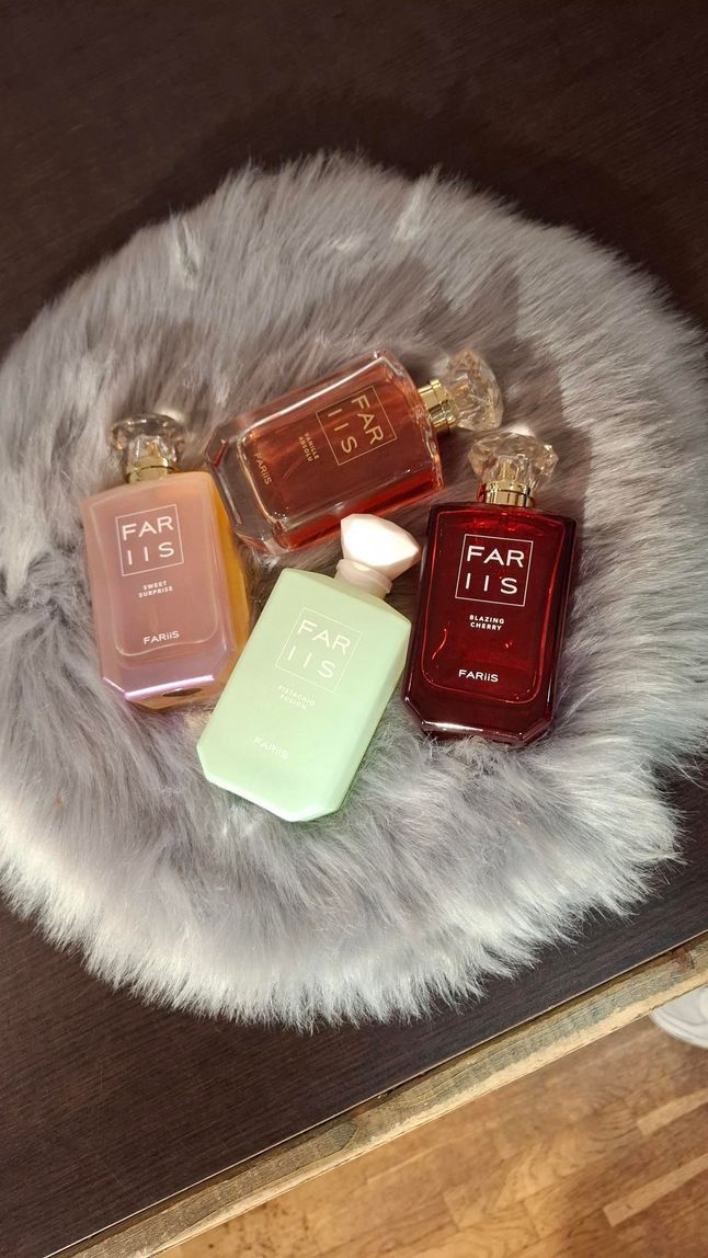 Vier flesjes Kayali-parfum in verschillende kleuren staan uitgestald op een rond, grijs kleed van imitatiebont.