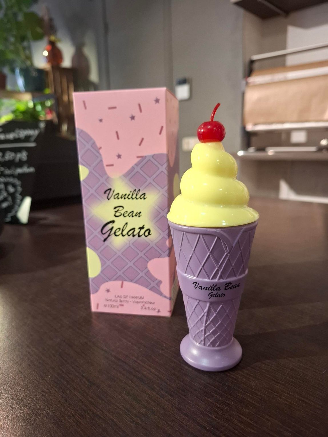 Paarse ijshoorn met gele swirls en een kers naast een pastelkleurig dessertdoosje op een tafel.