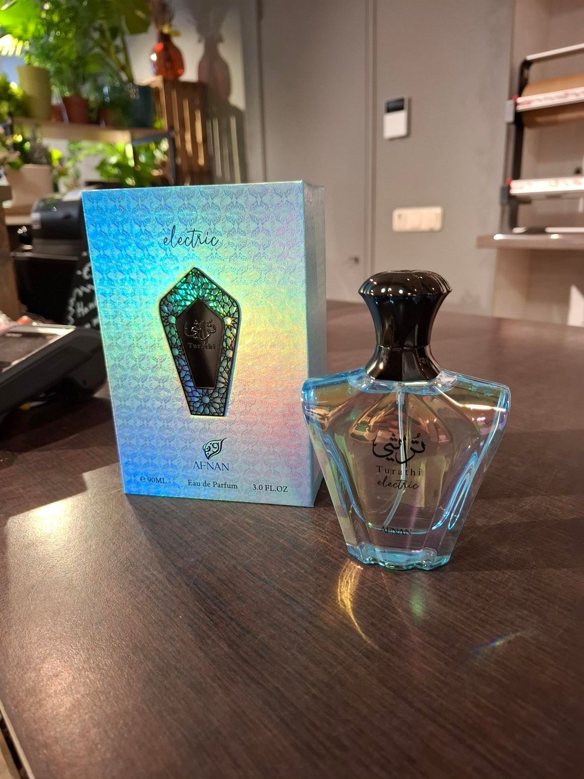 Een blauw parfumflesje naast de holografische doos op een tafel in een interieur.