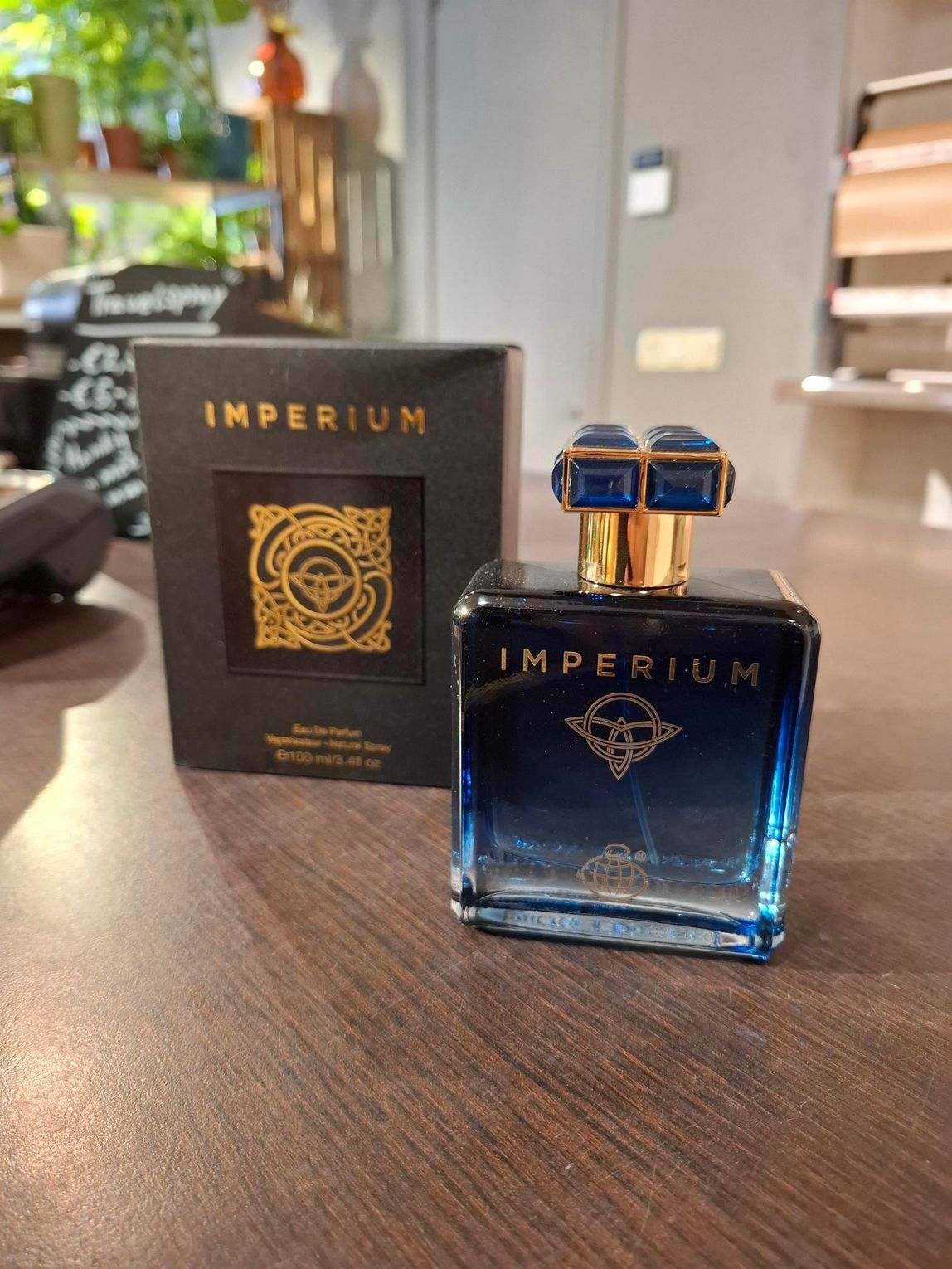 Parfumflesje en -doos van Imperium op een houten tafel, met blauw getint glas en gouden dop.