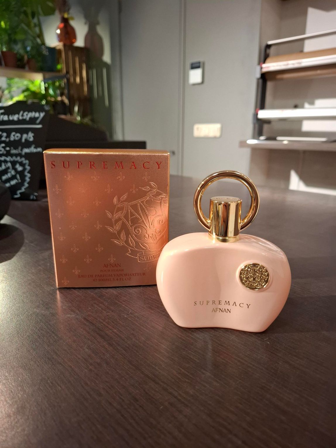 Roze parfumflesje met gouden ringdop naast een bruine ROJA-doos op een houten tafel