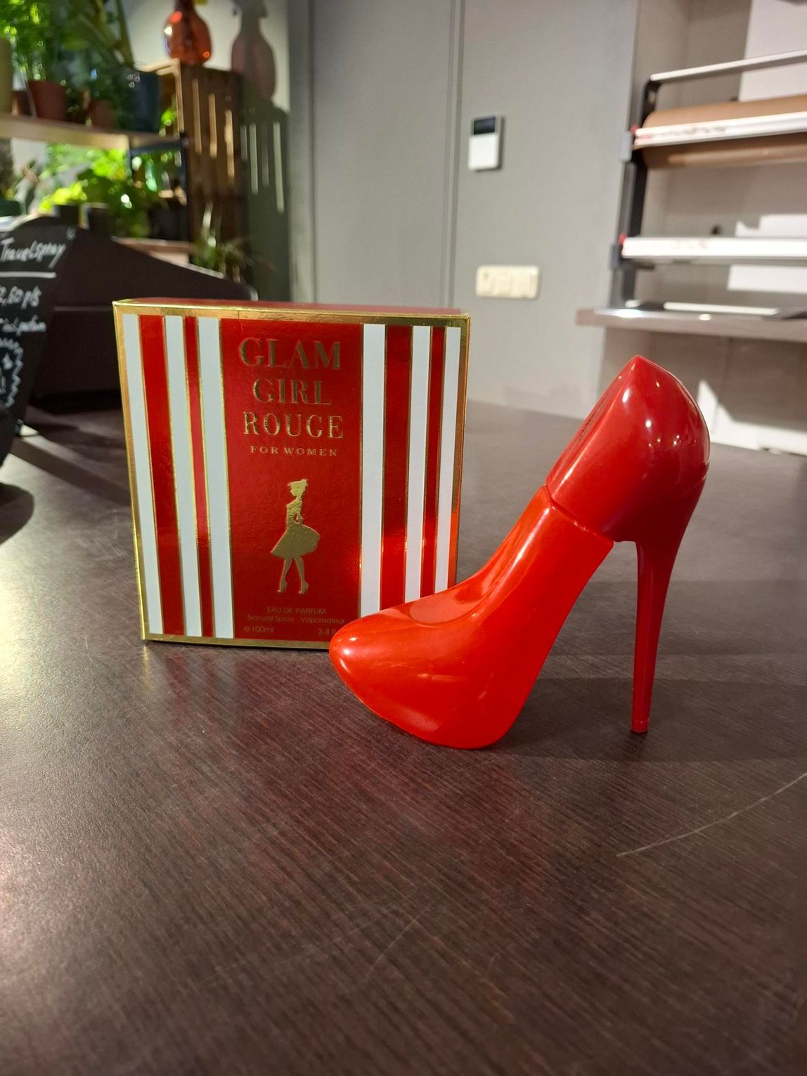 Een rode schoen met hoge hakken naast een gestreepte Glamour Rouge-doos op een tafel.