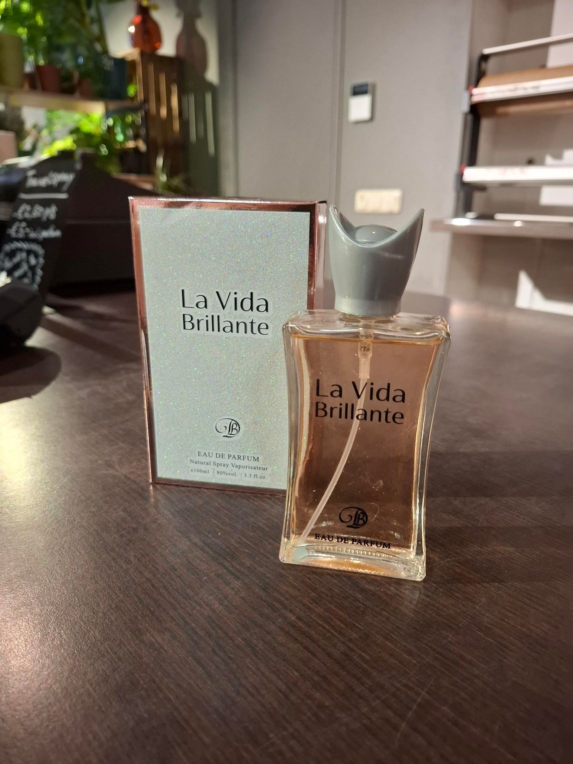 Parfumflesje en -doos van La Vida Brillante op een tafel met een wazige binnenachtergrond.