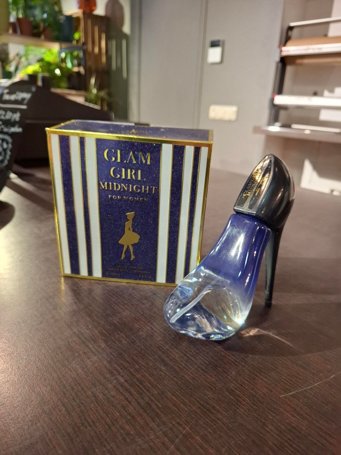 Een blauw glazen parfumflesje naast een gestreepte marineblauwe en gouden doos op een houten tafel.