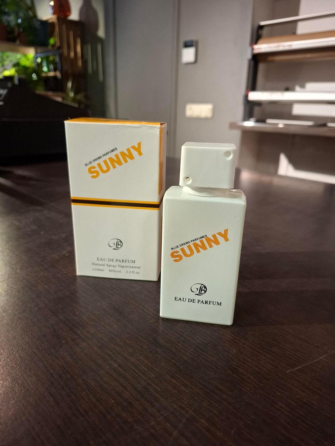 Twee witte SUNNY-parfumflesjes op een donkere tafel, met daarachter een doos.