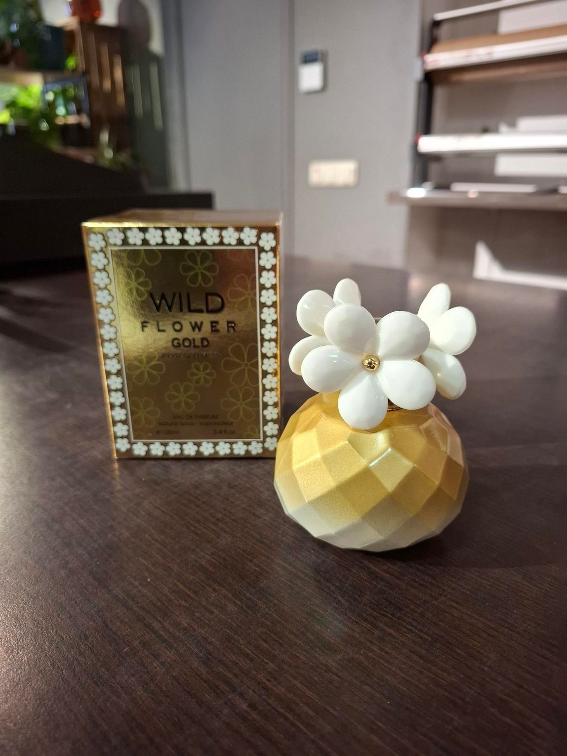 Parfumflesje en bijpassend doosje op een donkere tafel, met een klein decoratief wit bloempje.