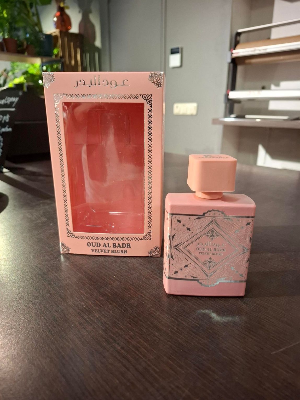 Roze parfumflesje naast een bijpassend doosje op een donkere tafel binnenshuis.