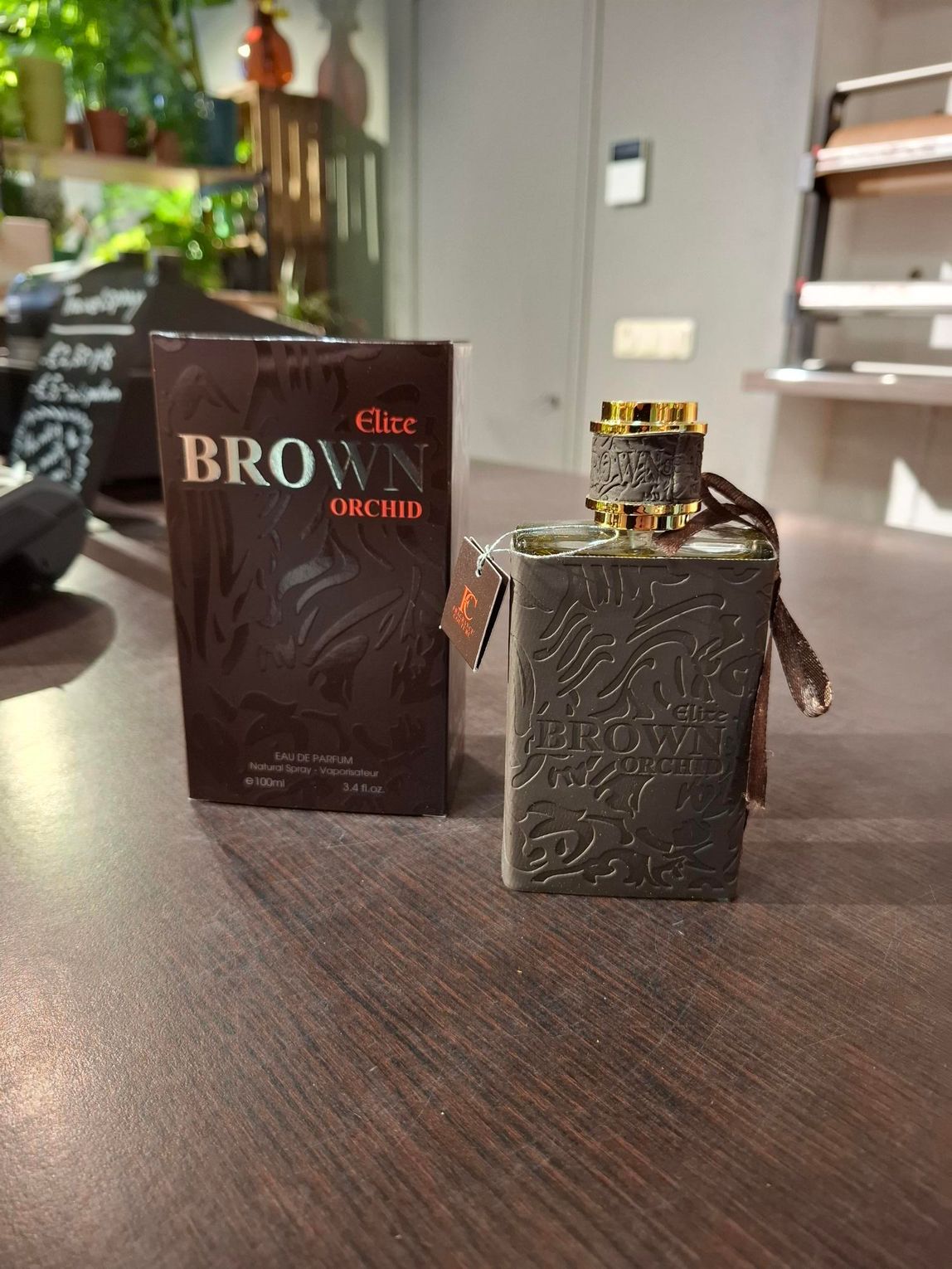 Twee parfumflesjes op een houten tafel, een zwart doosje en een vierkant metalen flesje met gouden dop.