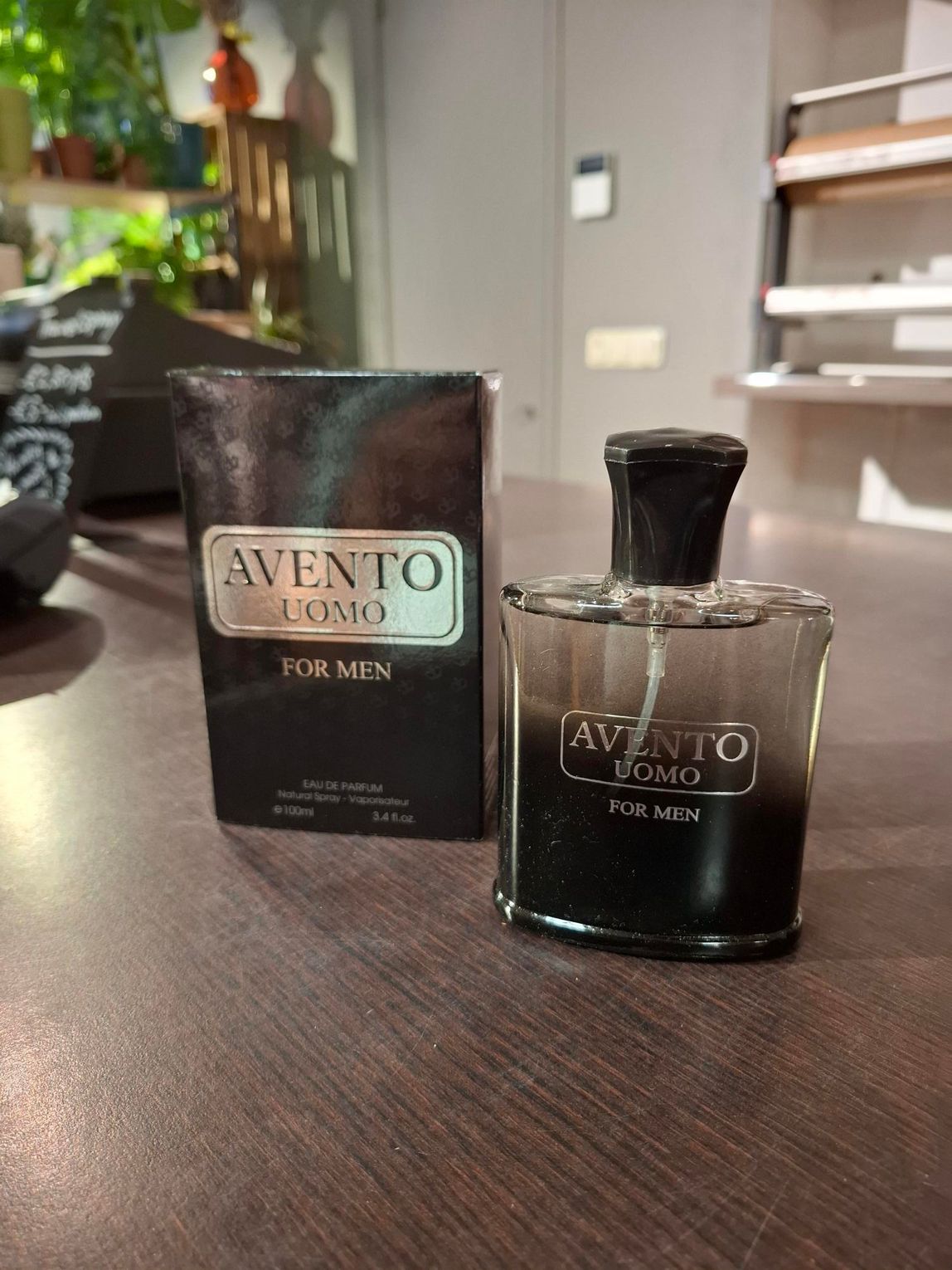 Een flesje Avento Uomo herenparfum naast de zwarte doos op een houten tafel.