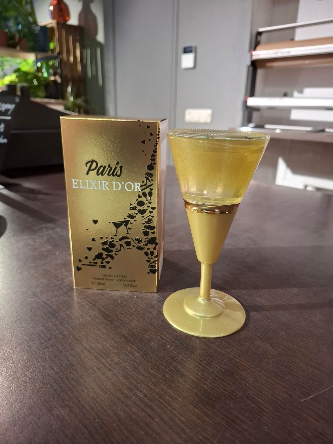 Een gouden doos Pura El D'orzo-drank naast een klein glaasje met een lichtgele drank op een tafel.
