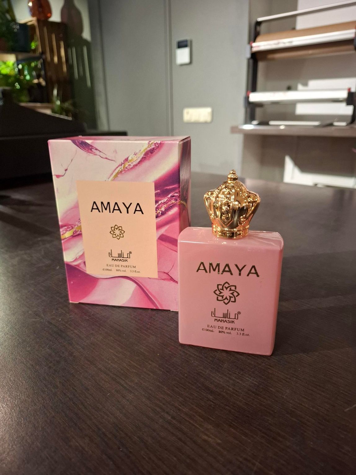 Roze AMAYA parfumflesje met bijpassend doosje op een donkere tafel in een kamer.