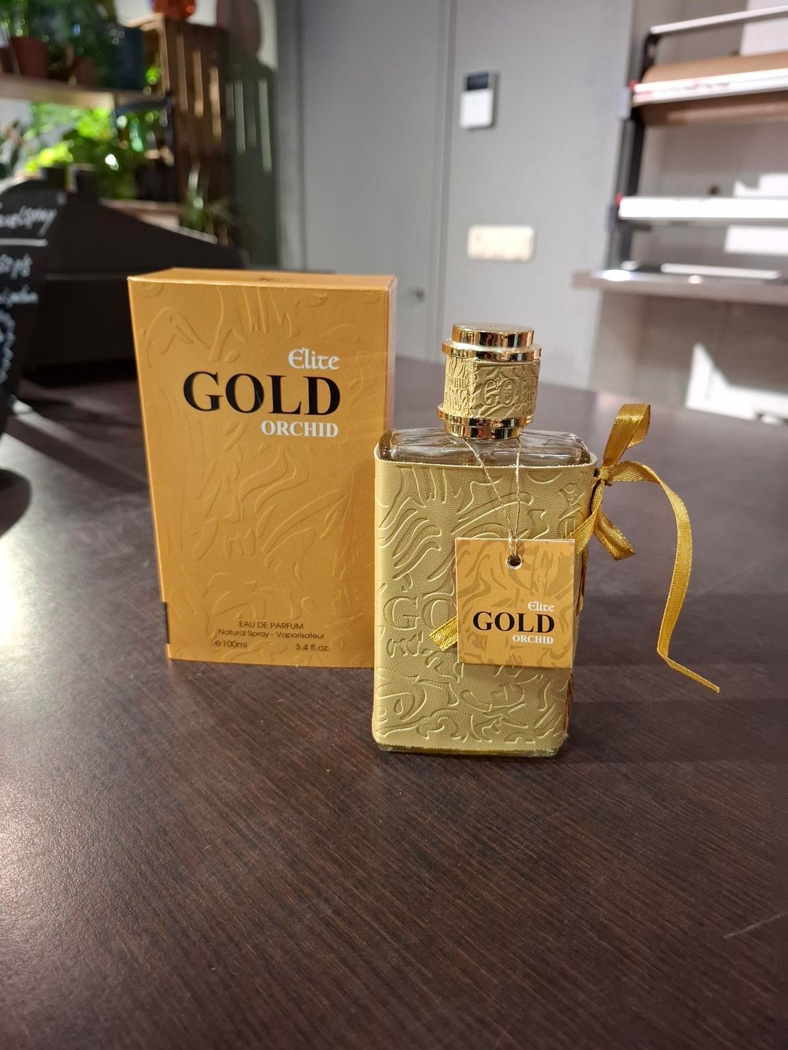 Gouden parfumflesje met bijpassend doosje op een donkere tafel.