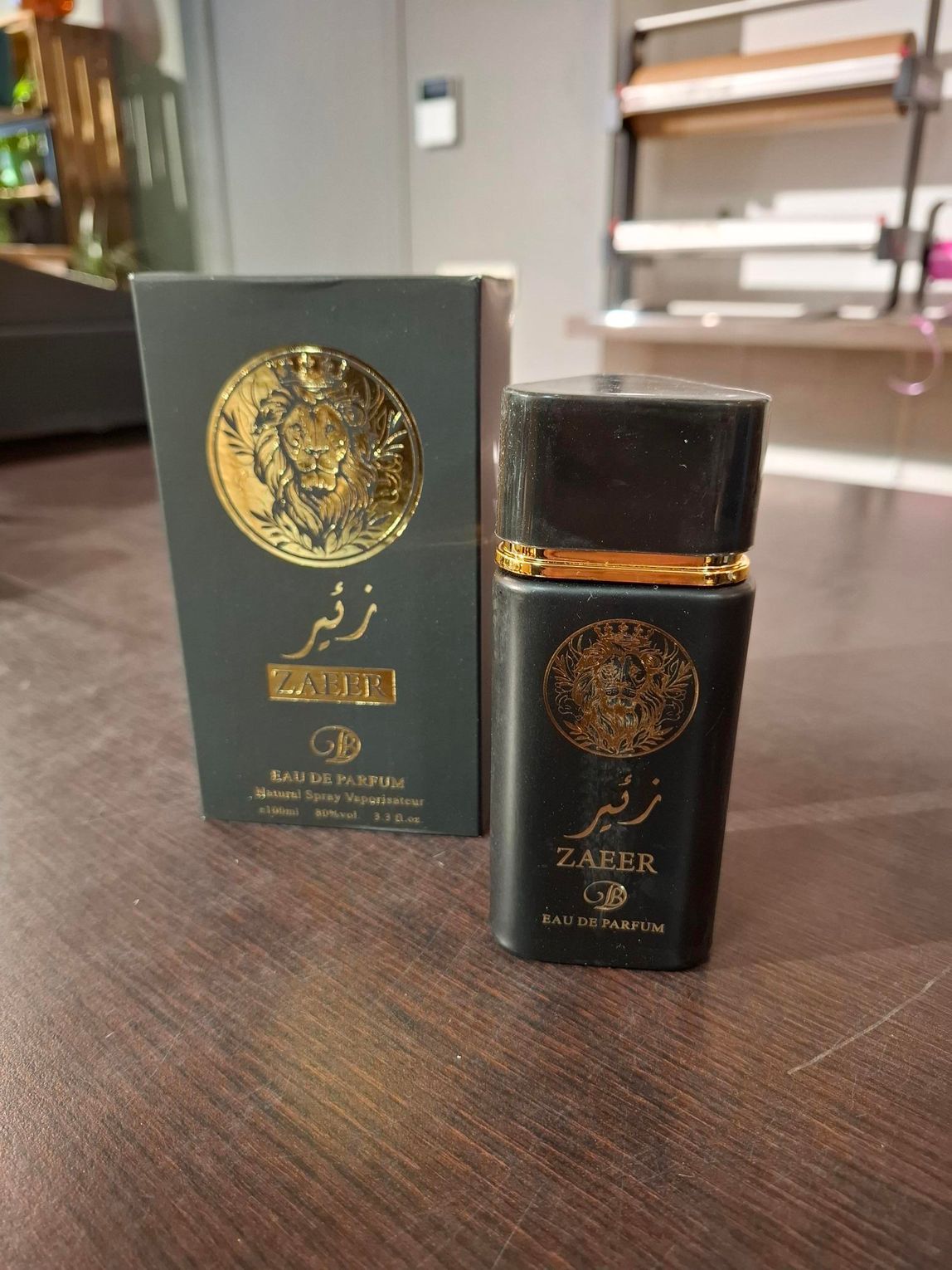 Zwarte parfumfles en bijpassende doos op een houten tafel, met gouden details en Arabische tekst.