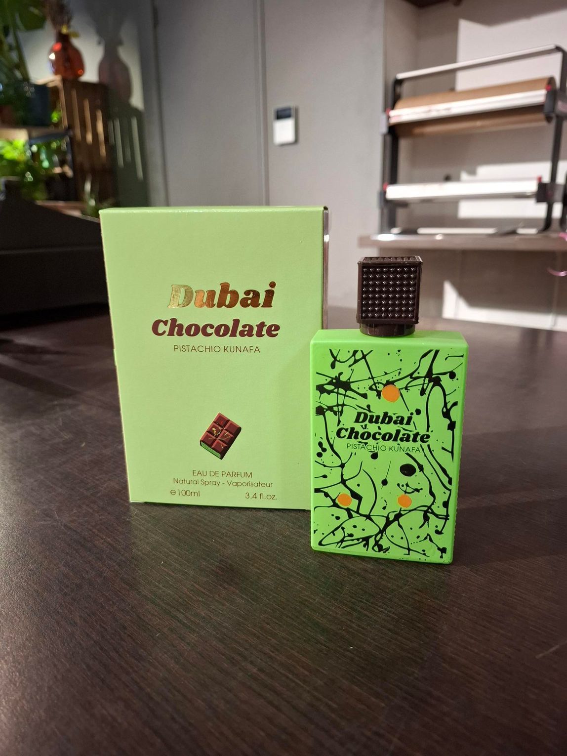 Op een tafel staan twee groene chocoladedozen, een grotere doos achter een kleinere met een stuk chocolade erop.