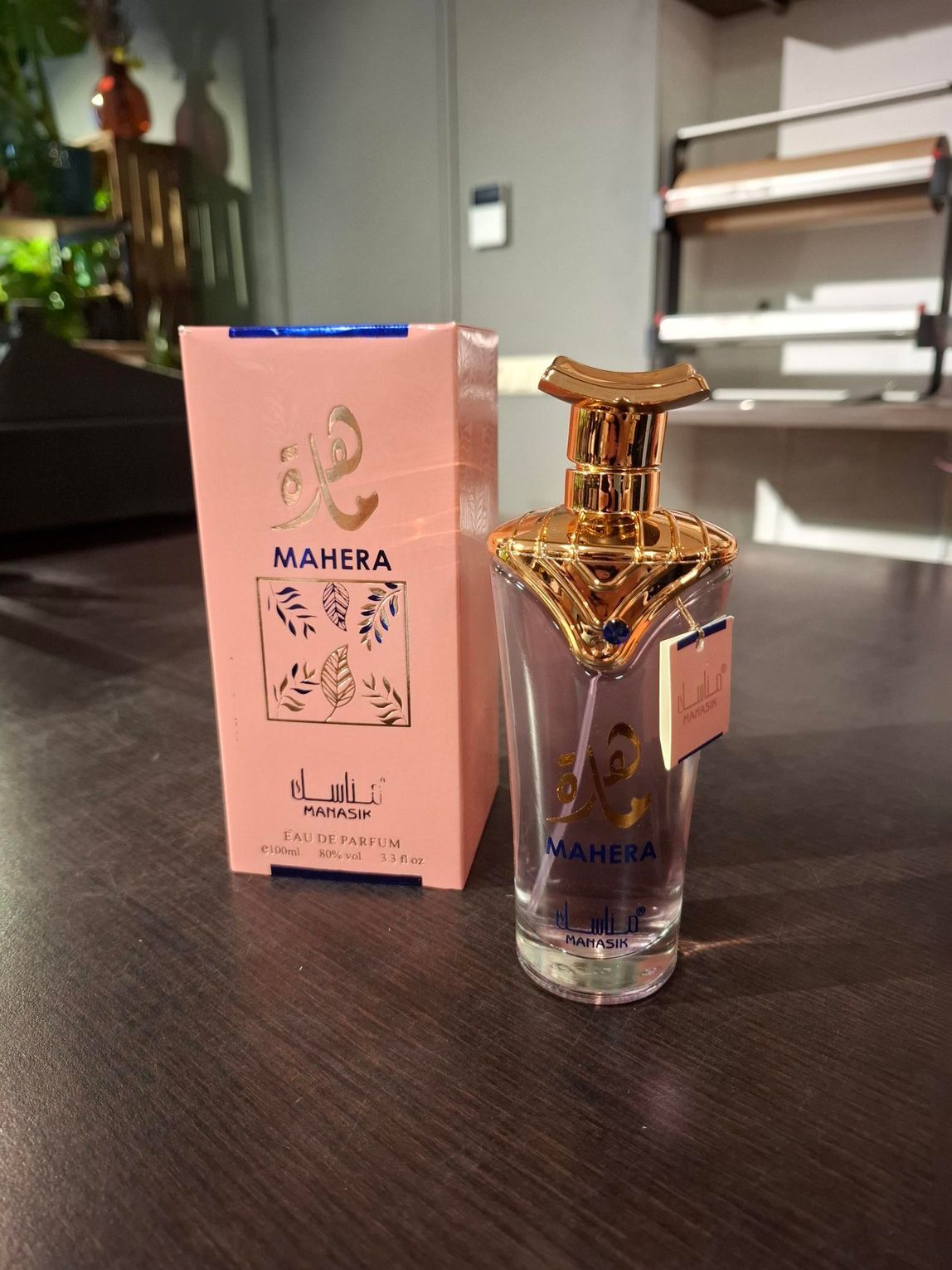 Roze MAHERA parfumdoos en sierlijke fles met gouden dop op een donkere tafel.