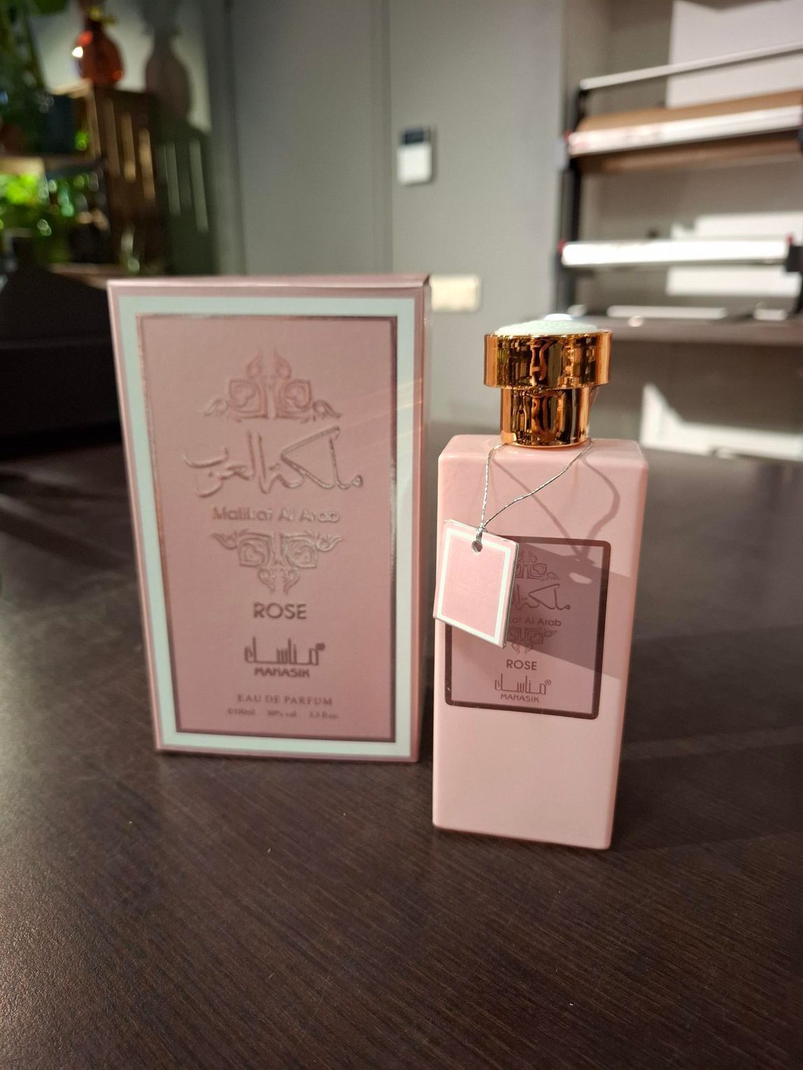 Een roze parfumflesje naast het bijpassende doosje op een donkere tafel, met een gouden dop en een zachte, bloemige verpakking.