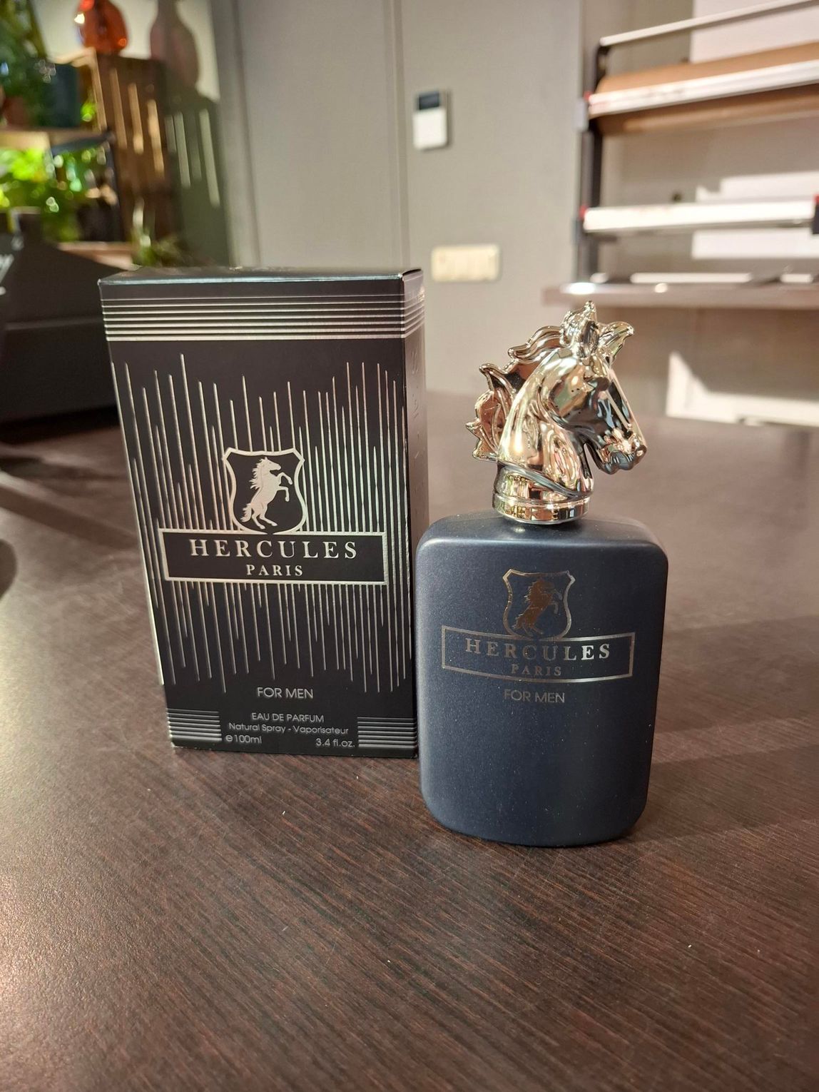 Zwarte parfumfles met sierlijke zilveren dop naast een bijpassende doos op een houten tafel.