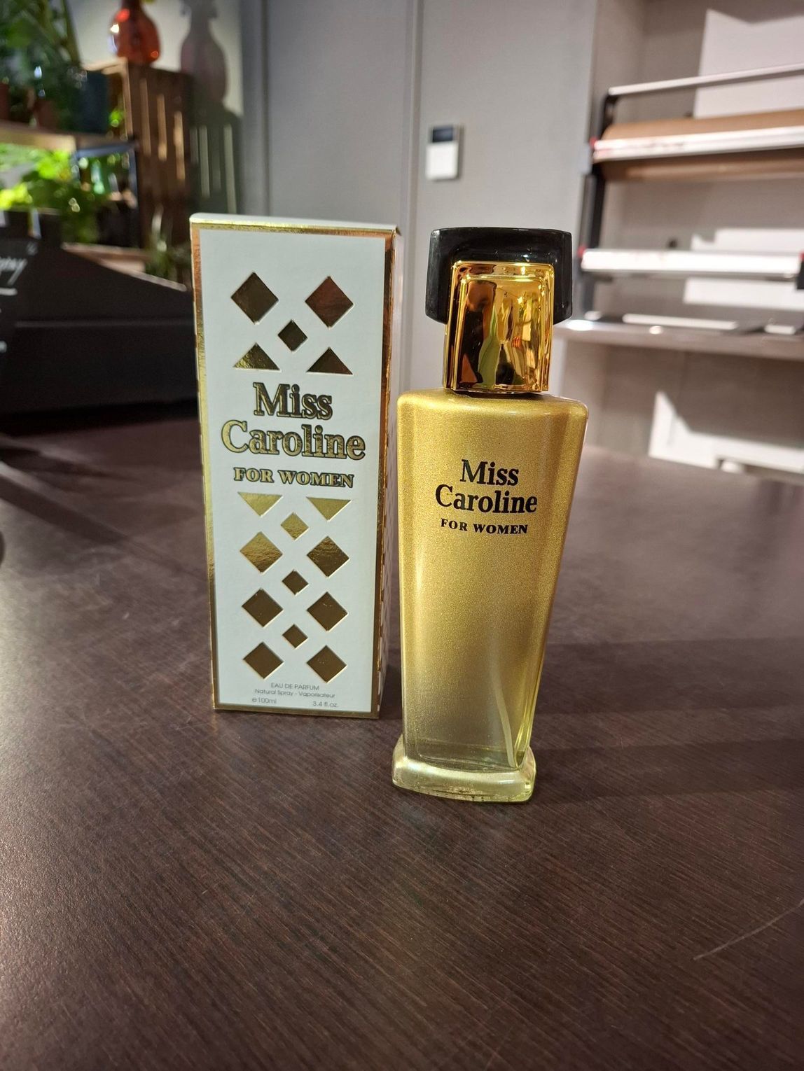 Het parfumflesje Mits Caroline staat naast de wit-gouden doos op een tafel.