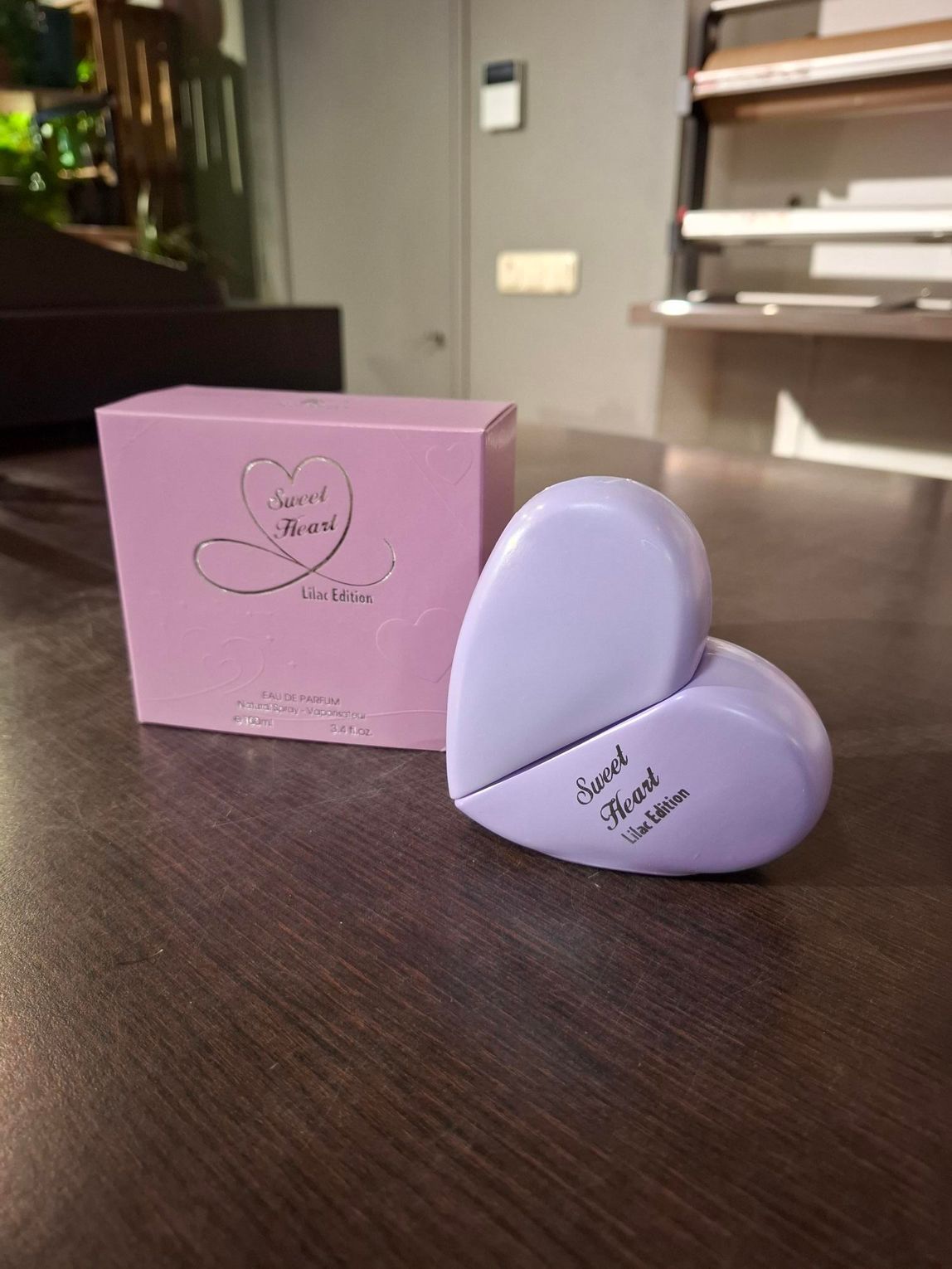 Een lavendelkleurig hartvormig doosje en een compact doosje op een houten vloer naast een roze doosje.