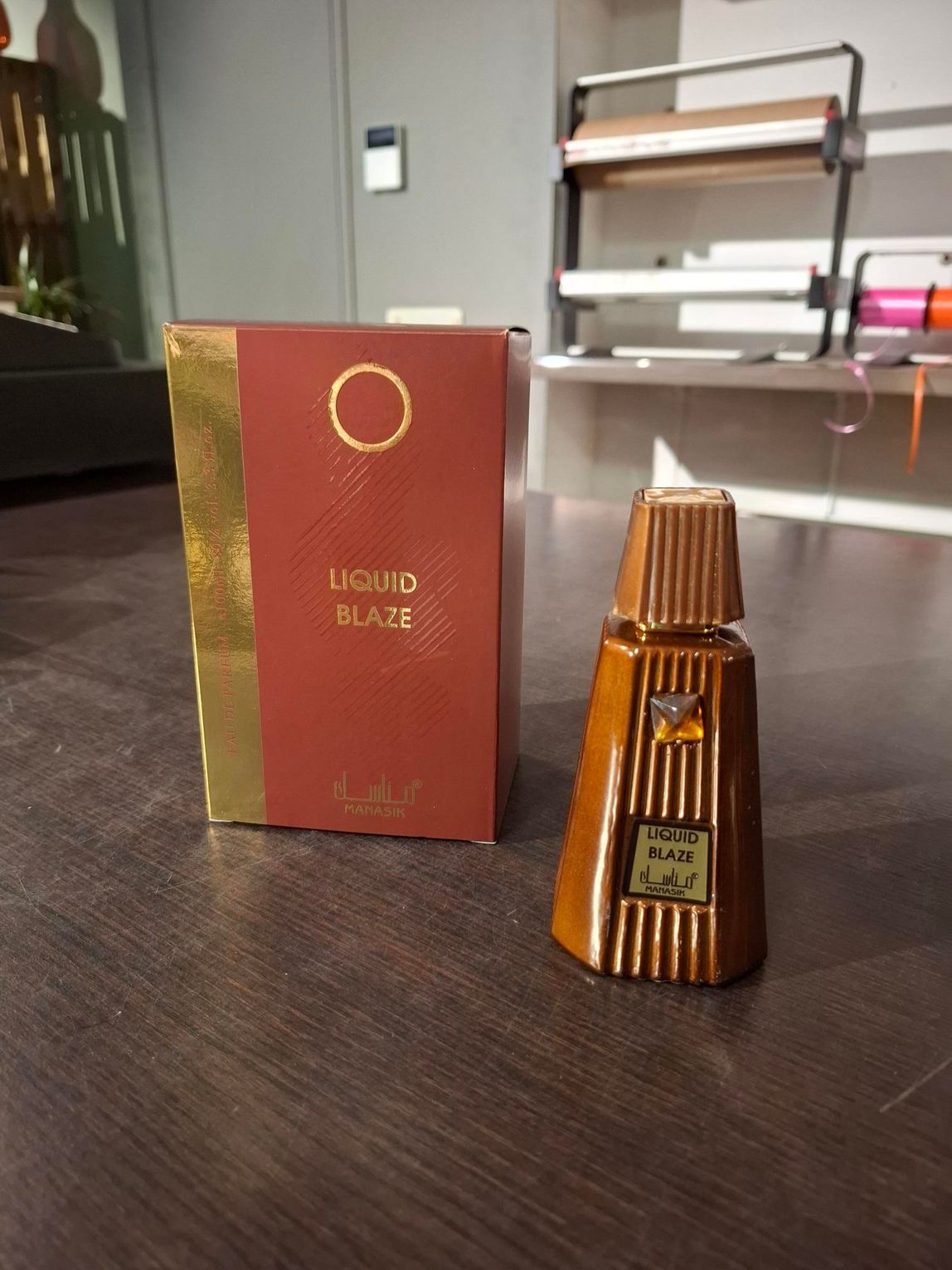 Een parfumflesje met bruine strepen naast een bijpassende rood-gouden doos op een tafel binnen.