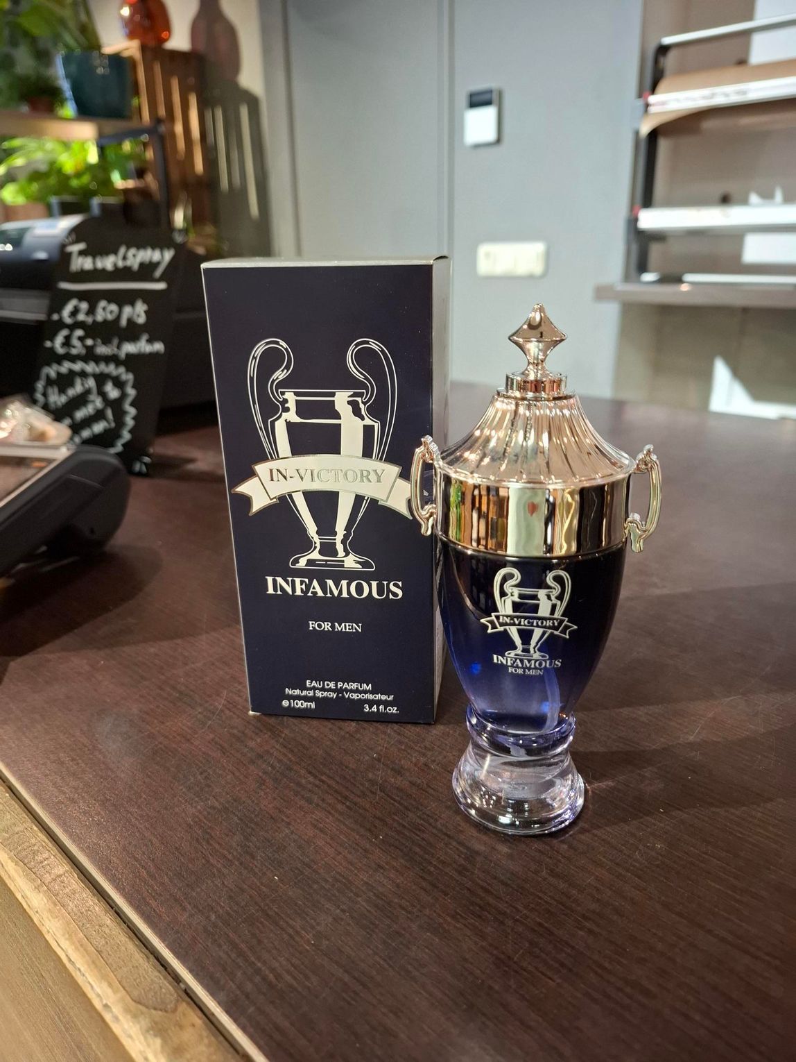 Een blauw-gouden parfumflesje naast de zwarte geschenkverpakking op een tafel.