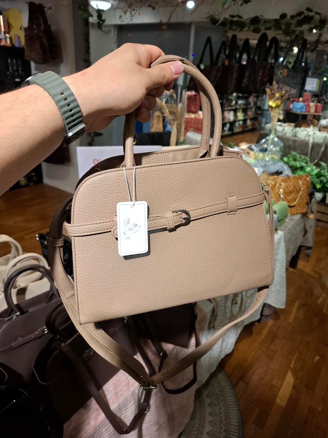 Hand die een beige handtas met prijskaartje vasthoudt in een winkelvitrine.