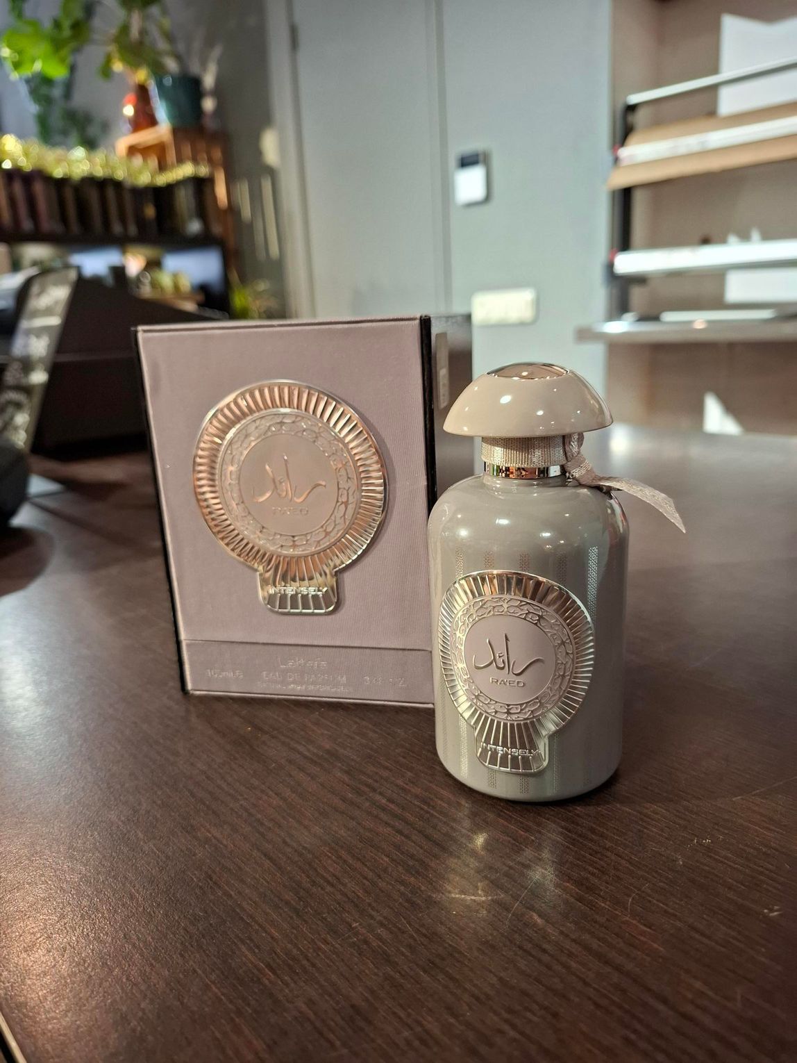 Een klein grijs parfumflesje naast de doos op een donkere tafel in een zacht verlichte kamer.