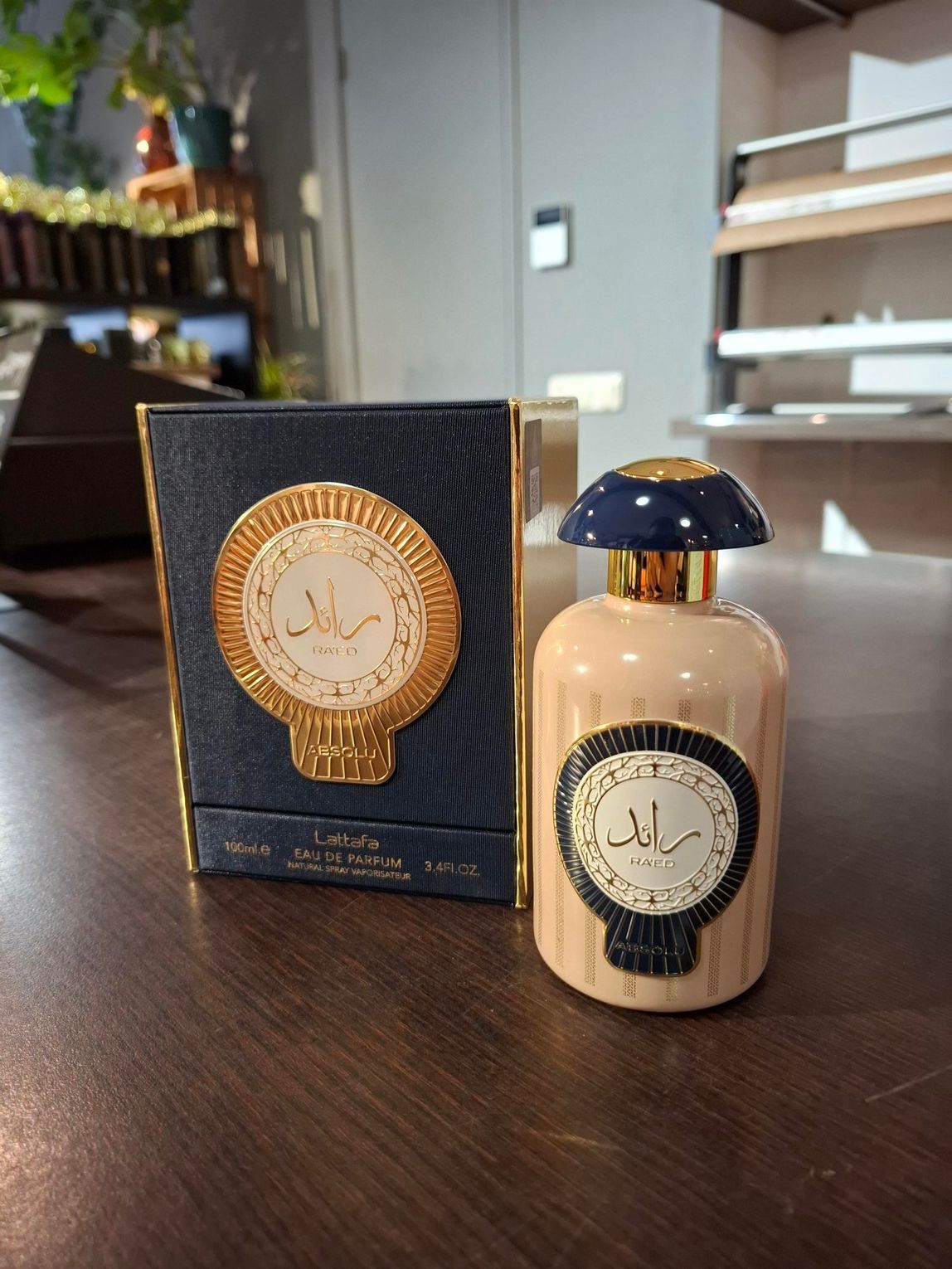 Parfumflesje met zwarte dop naast een bijpassende zwart-gouden doos op een tafel.