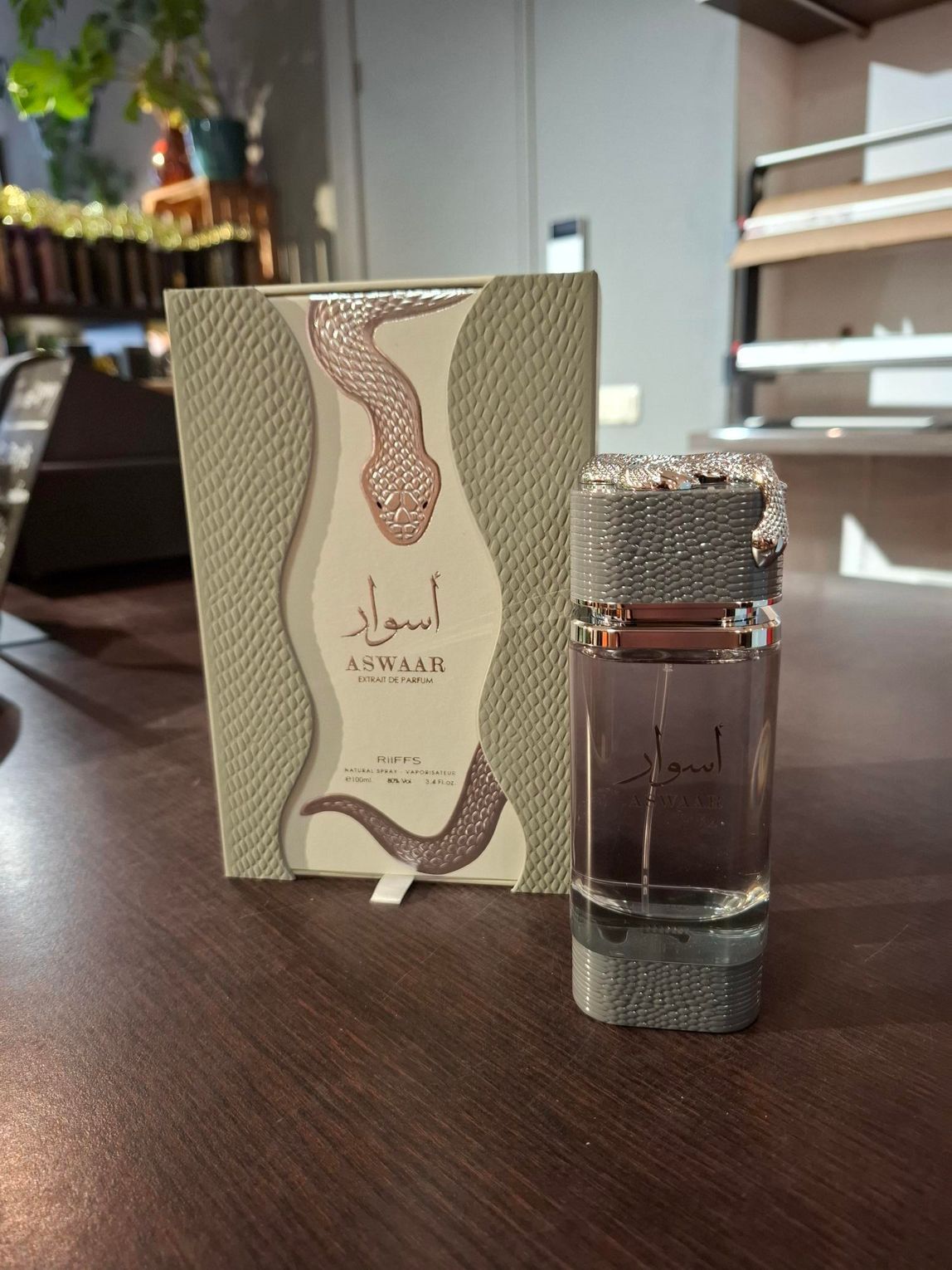 Parfumflesje met decoratieve zilveren dop naast het bijpassende doosje op een houten tafel.
