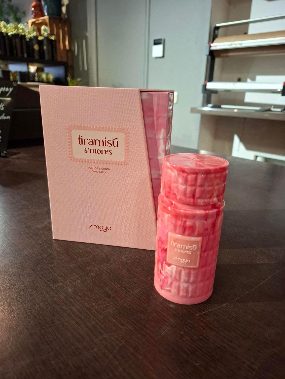 Roze productdoos en bijpassende cilindervormige container op een donkere tafel, met planken op de achtergrond.