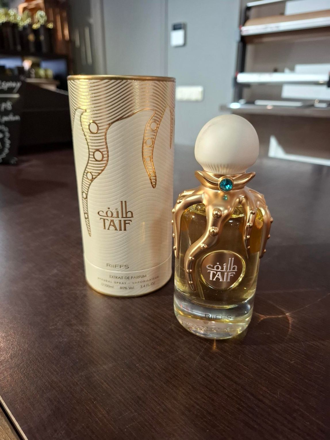 Gouden parfumflesje en bijpassend cilindervormig doosje op een donkerhouten tafel.