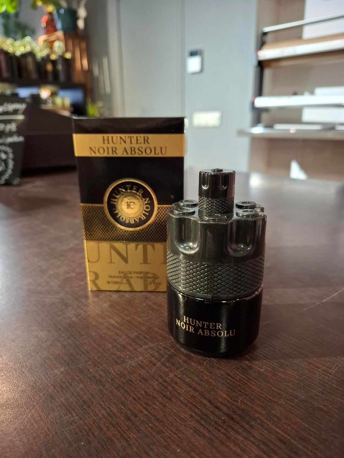 Een zwart parfumflesje met gouden dop staat naast een geel doosje Hunter for Men op een tafel.