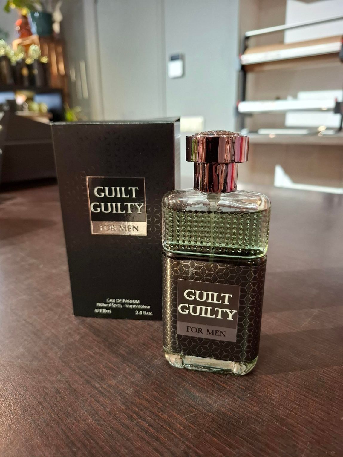 Parfumflesje en -doosje van Guilt op een houten tafel, met een wazige achtergrond van de kamer.