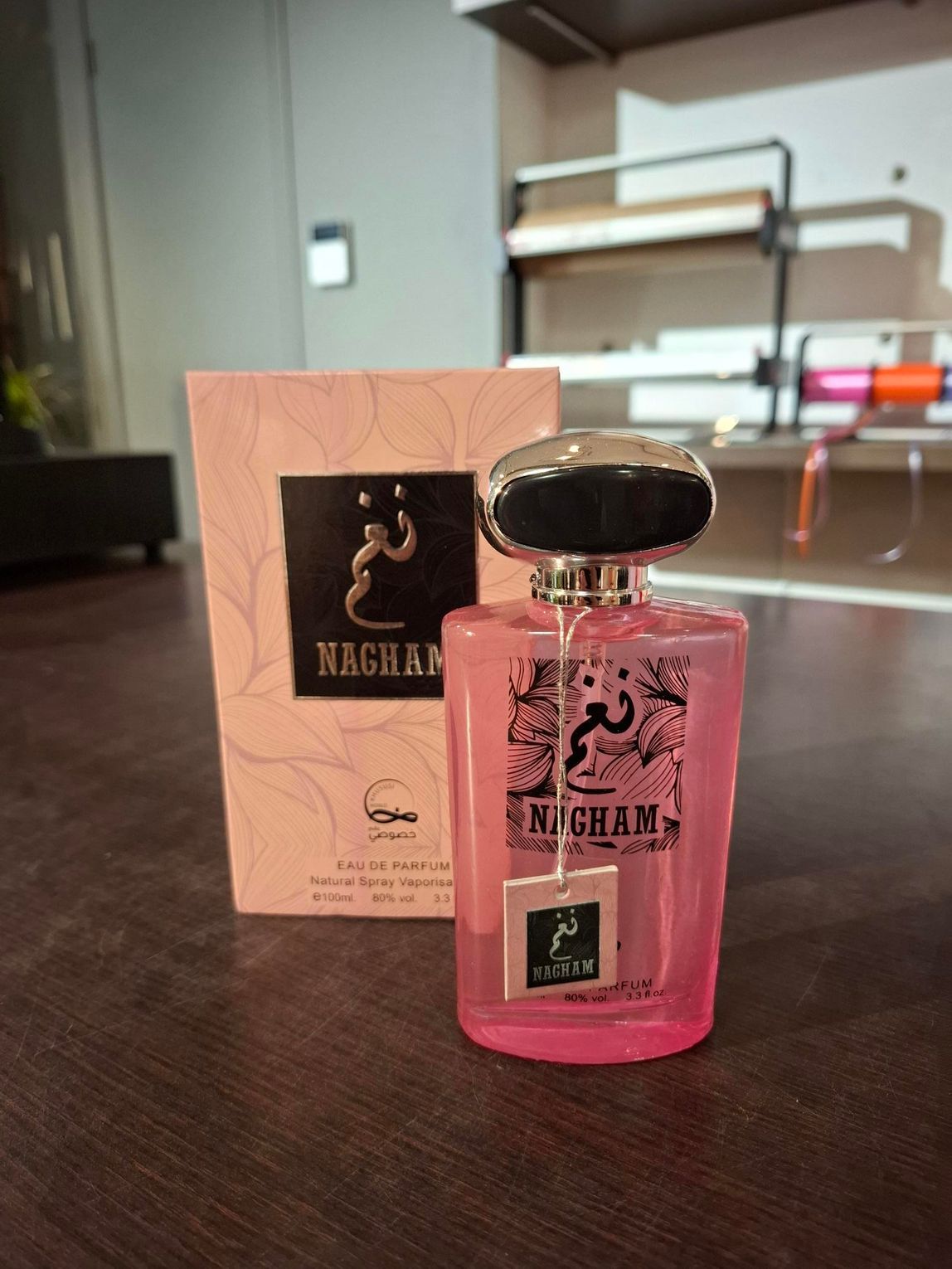 Roze parfumflesje met gouden dop naast een bijpassend doosje op een tafel.