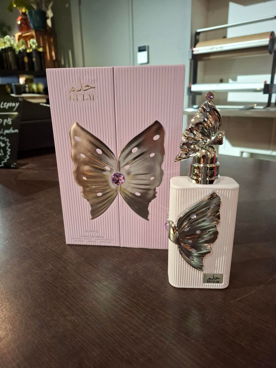 Een roze cadeautas met vlinderversiering en een bijpassende doos op een tafel, samen met een klein decoratief beeldje.