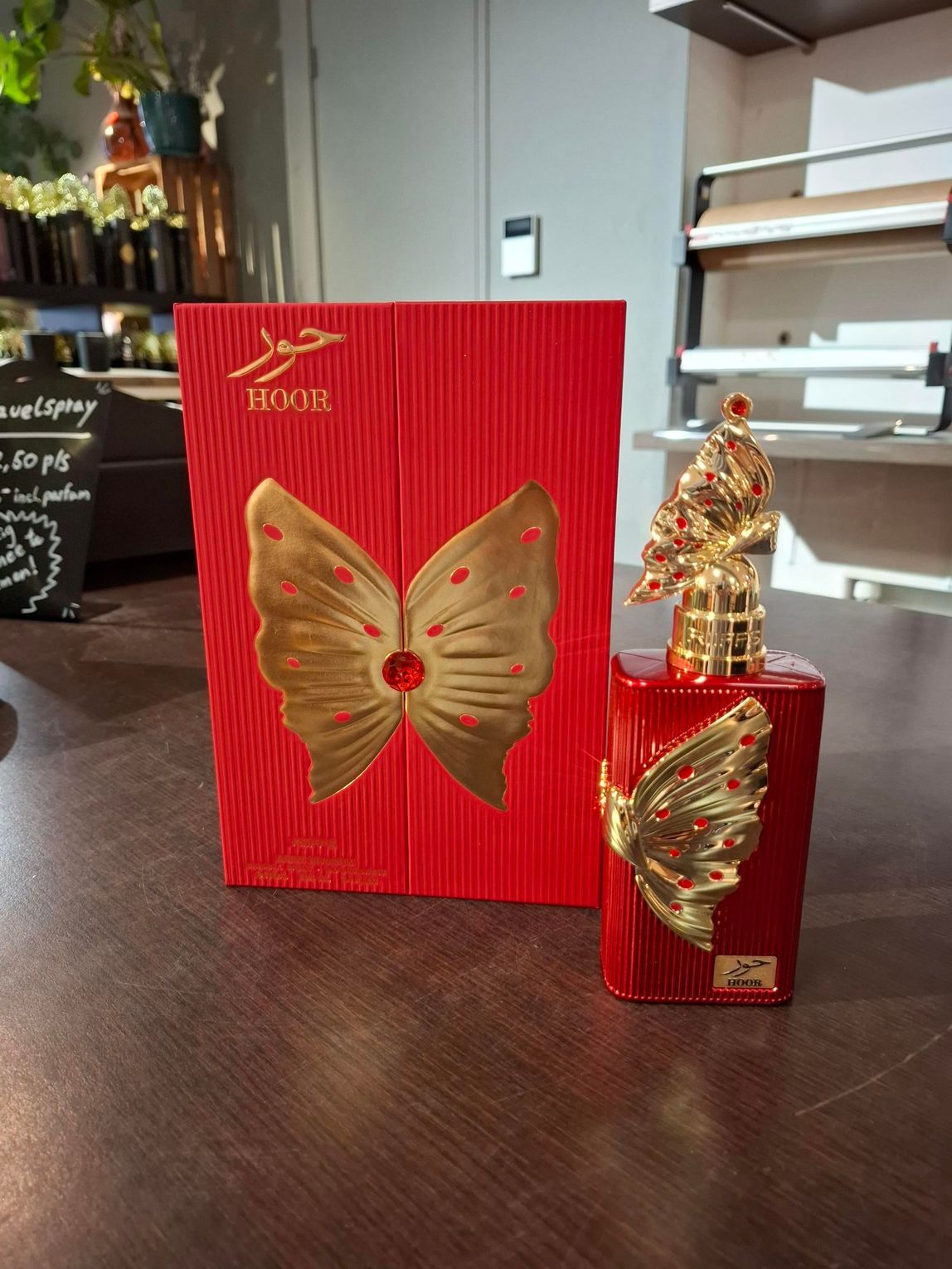 Een rode cadeautas met vlindermotief en een bijpassende rode doos met gouden vlinderaccenten op een houten tafel.