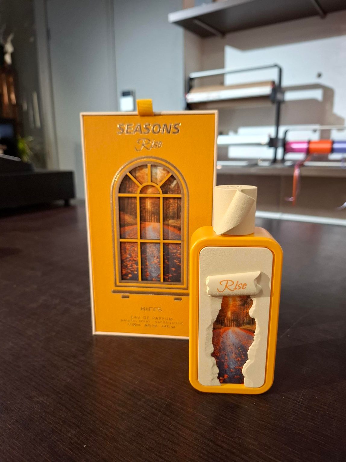 Een oranje parfumflesje met bijpassend doosje op een tafel, met een wazige kamer op de achtergrond.