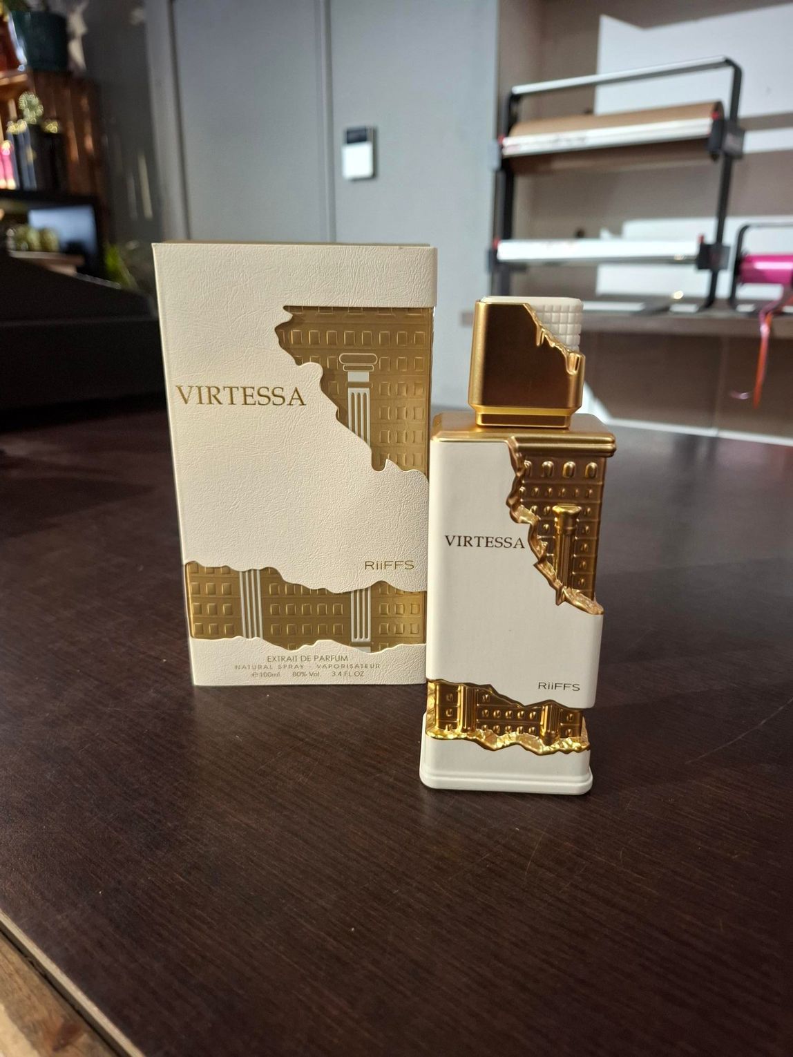 Goud-witte parfumfles naast het bijbehorende doosje op een donkere tafel in een kamer.