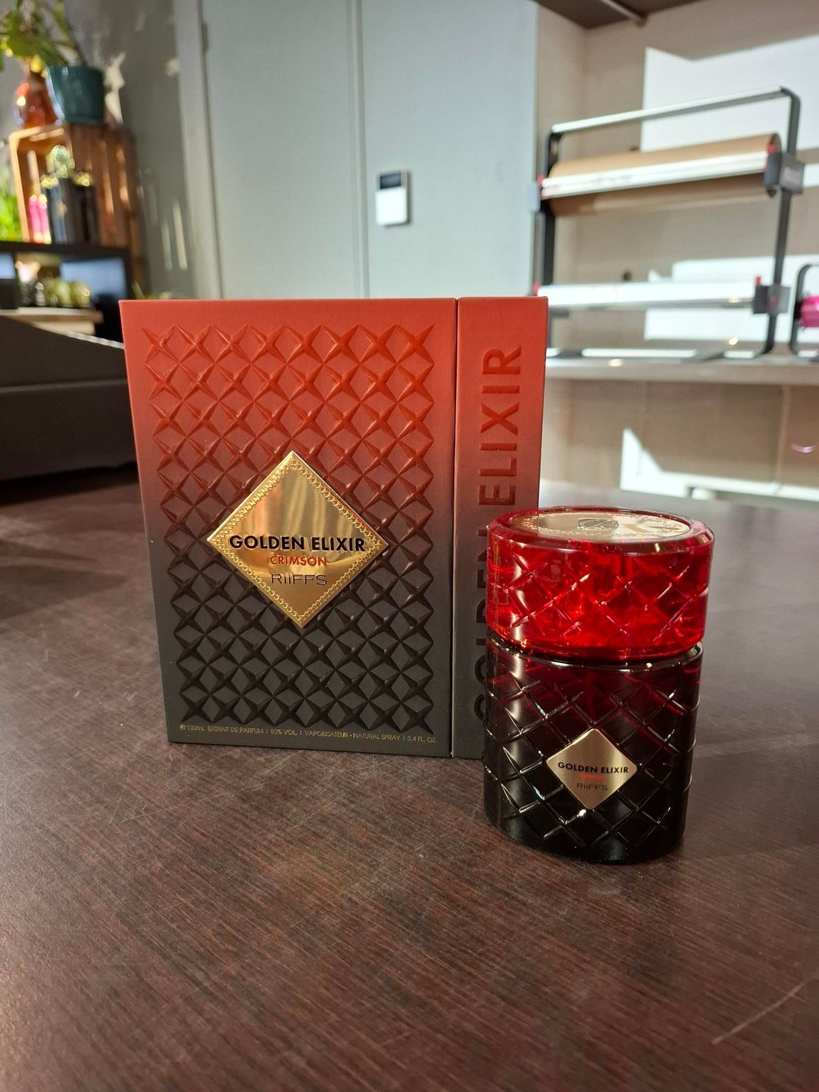 Parfumflesje en doosje van Red Elixir op een tafel, met donkerrood glas en oranje-rode verpakking.