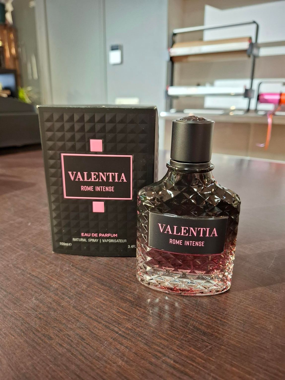 Parfumflesje en -doos van Valentia op een houten tafel, met roze vloeistof en zwarte dop.