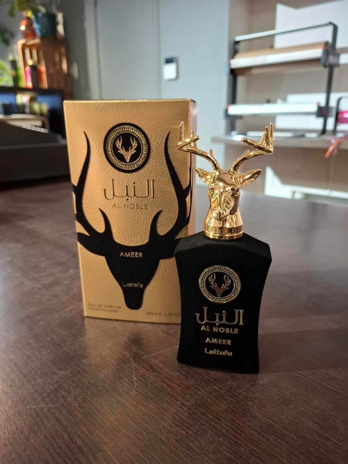Zwarte parfumfles met gouden hertenkopdop naast een bijpassende gouden doos op een houten tafel.