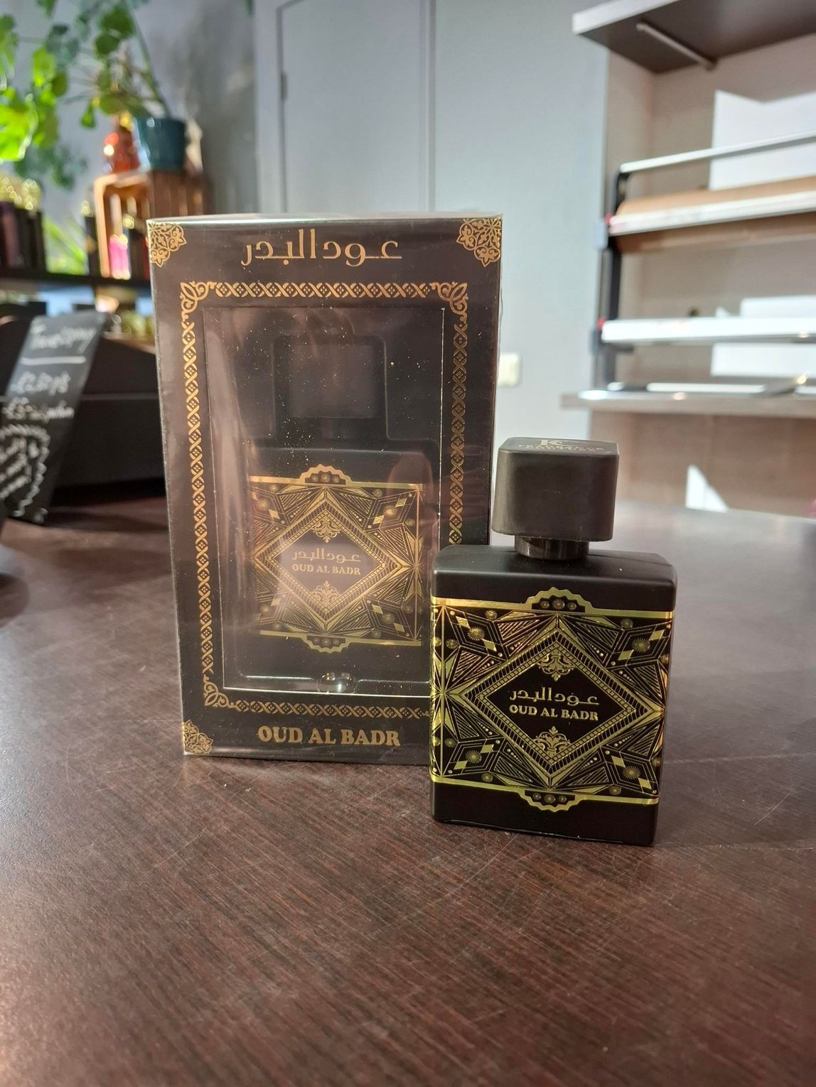 Parfumflesje en -doos met gouden Arabische letters op een houten tafel.