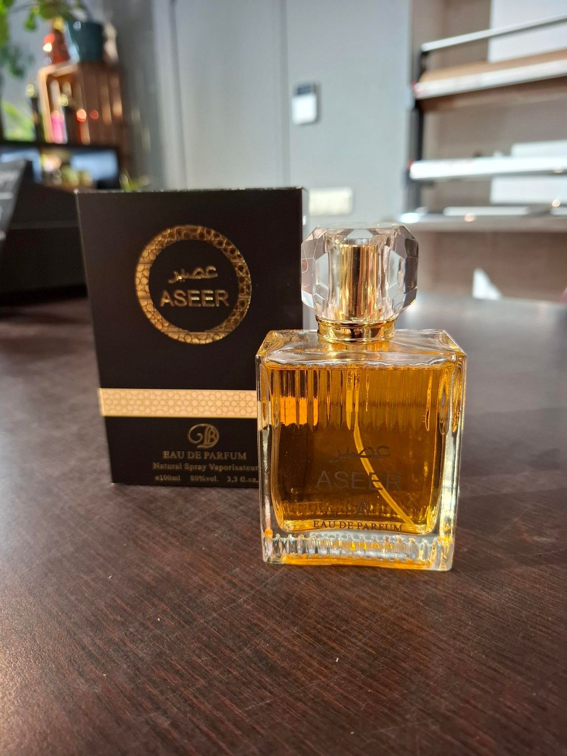 Een amberkleurige parfumfles en een zwarte ASER-doos op een tafel in een wazige binnenomgeving.