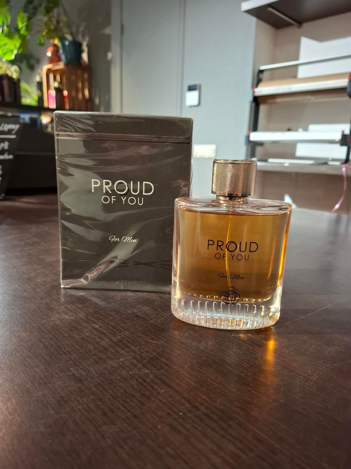 Een fles en doos PROUD-parfum op een houten tafel, met planken op de achtergrond.