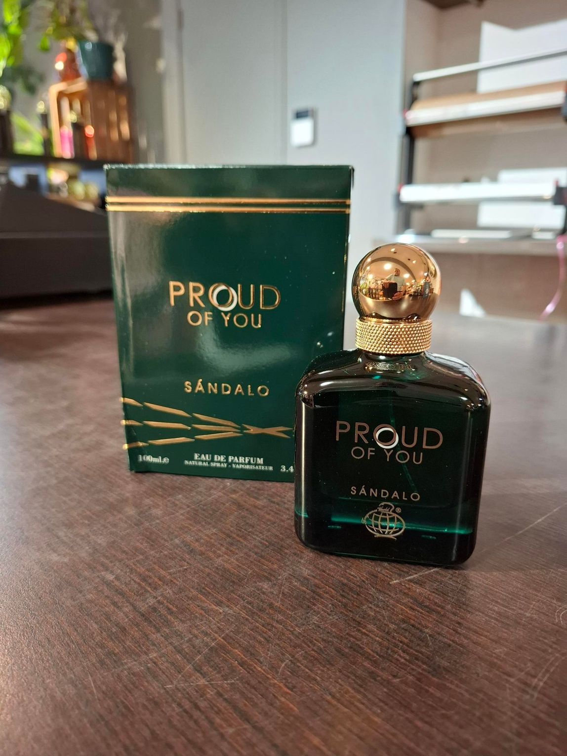 Groen-gouden parfumflesje met bijpassend doosje op een houten tafel.